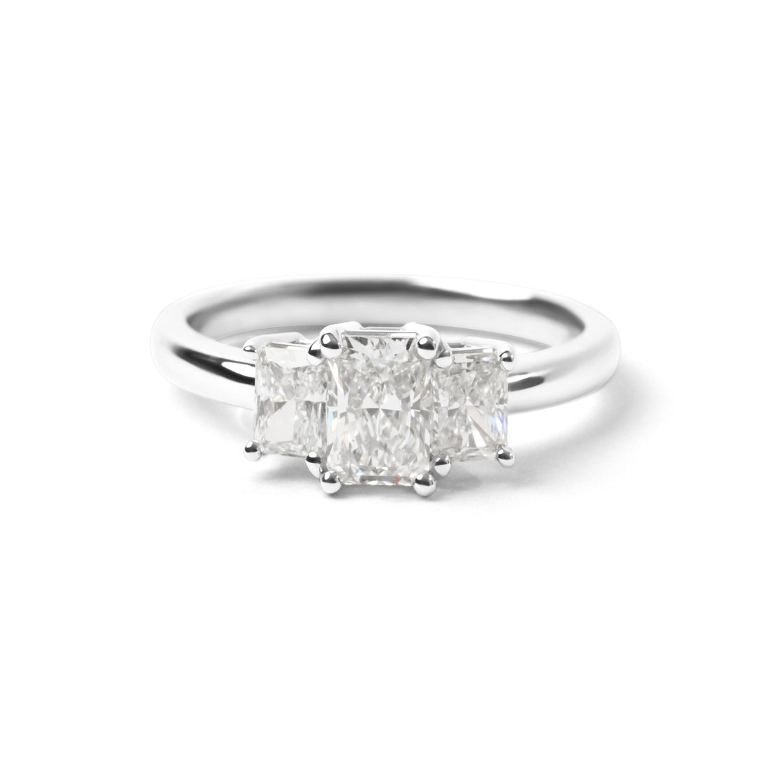 A three-stone diamond ring featuring a center radiant-cut diamond flanked by two smaller round-cut diamonds, set in a polished silver-colored band on a clean white background.