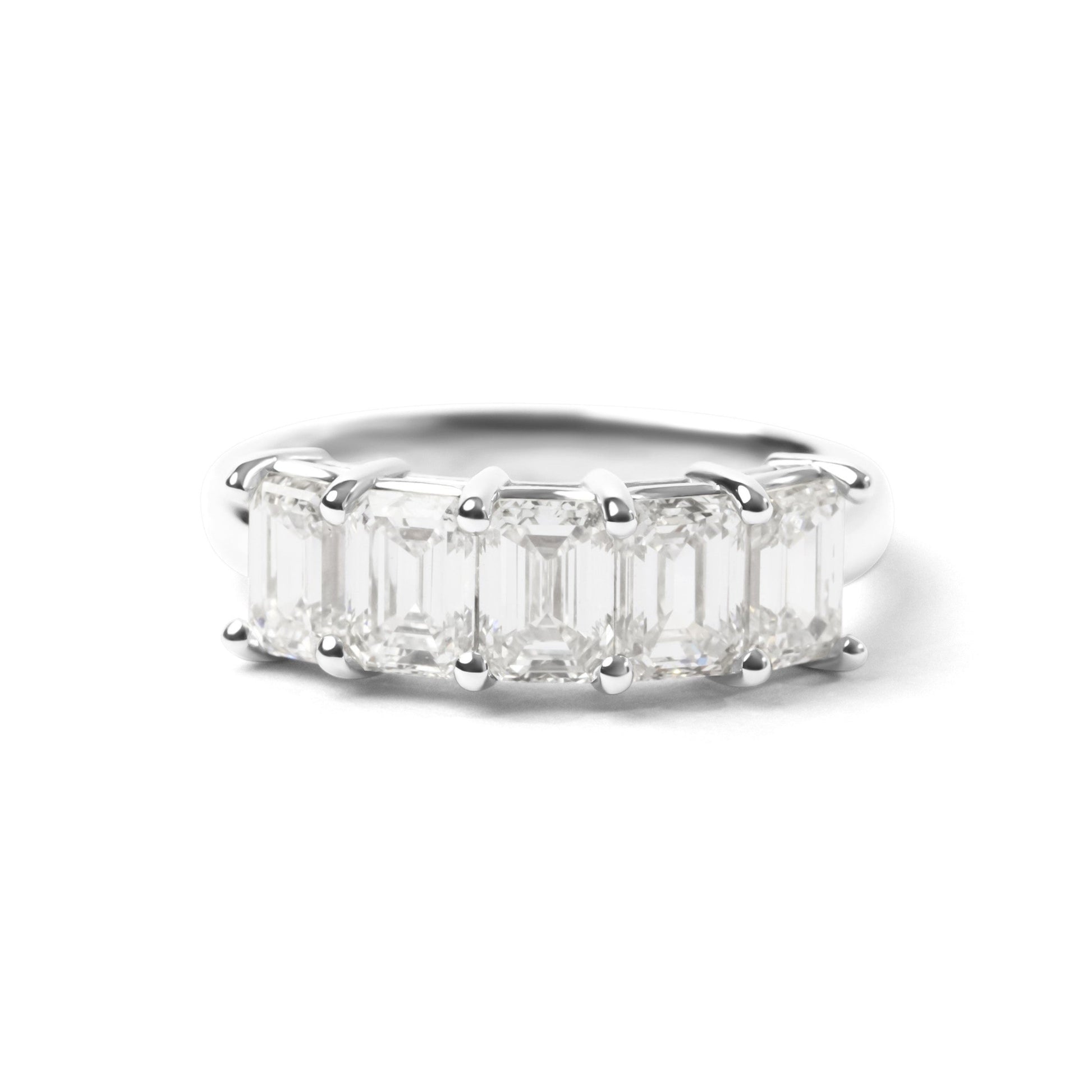 A silver band ring featuring a row of emerald-cut clear gemstones in a prong setting, shown against a plain white background.