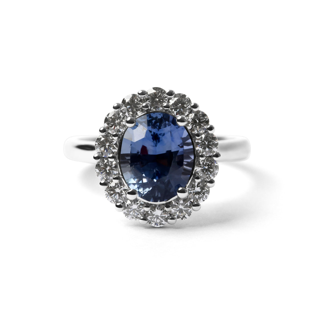 A silver ring featuring a large oval-cut deep blue sapphire gemstone surrounded by a halo of small clear stones, set against a plain white background.