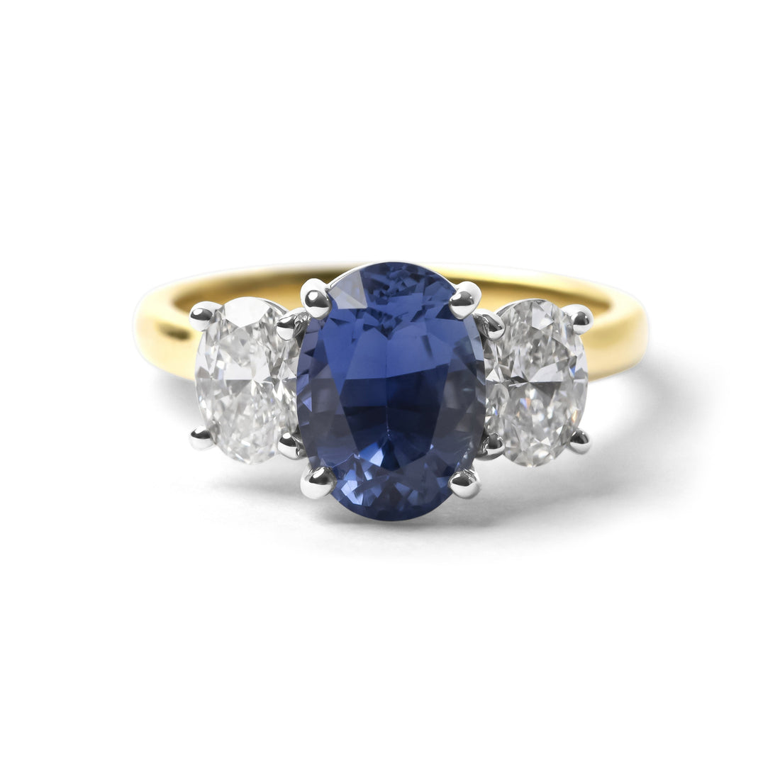 A three-stone ring featuring a central oval-cut deep blue sapphire flanked by two round-cut clear diamonds on a yellow gold band, set against a plain white background.
